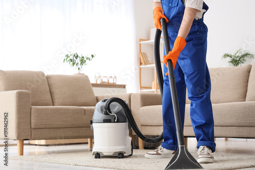 Cuadro en lienzo Male janitor with modern vacuum cleaner cleaning carpet in living room