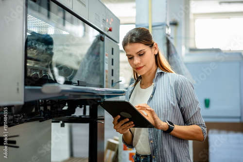 Foto Female worker inspecting machinery in printing factory, using digital tablet for monitoring production and quality control