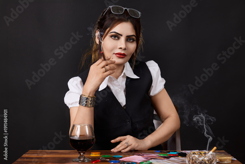 Portrait of a confident woman smoking at a gambling table with poker chips, playing cards and alcohol. Concept image illustrating high risk decisions, casino lifestyle, addiction, temptation 