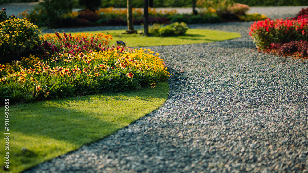 Fototapeta premium Beautiful landscape garden with winding gravel path and colorful flowers in morning sunlight
