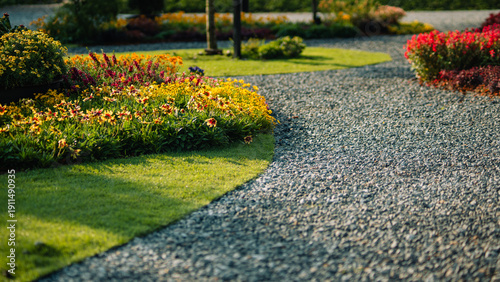 Beautiful landscape garden with winding gravel path and colorful flowers in morning sunlight