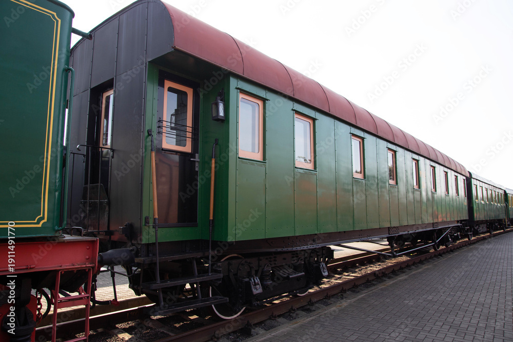 Fototapeta premium Historic green and red train carriage displayed in a railway museum during a sunny day
