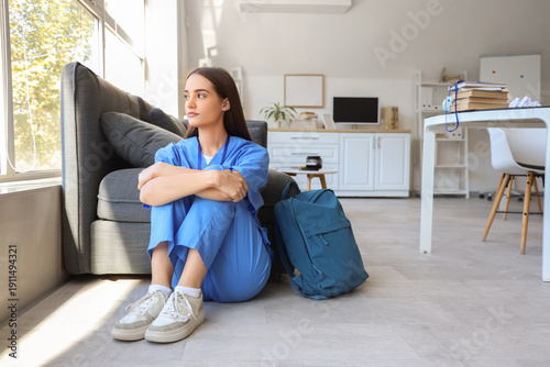 Upset female medical intern sitting on floor in clinic