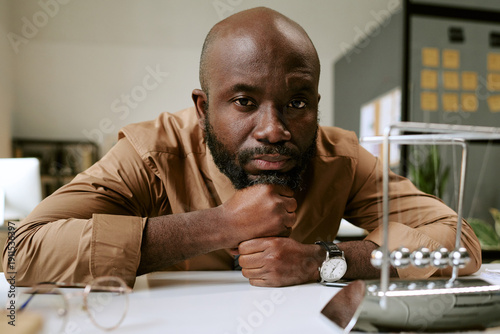Canvas Print Portrait of Black man sitting at desk resting chin on hand looking into camera w