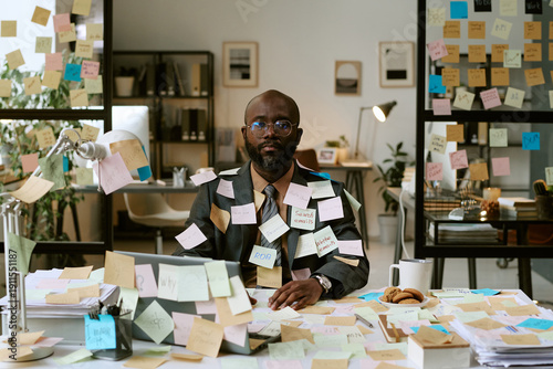 Foto Portrait of Black man sitting at cluttered office desk covered with sticky notes