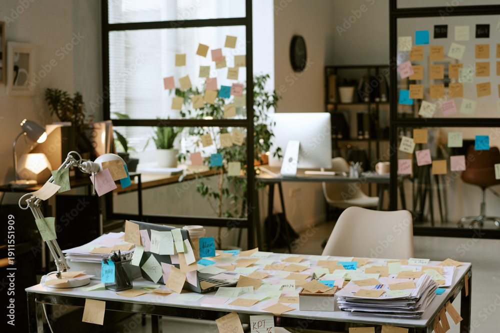 Obraz premium Modern office workspace covered with sticky notes on desk, glass walls, and computer monitor, showing business planning and brainstorming process in professional environment
