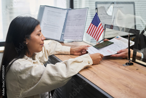 Fotografie Young adult Hispanic woman submitting documents to official behind counter at vi