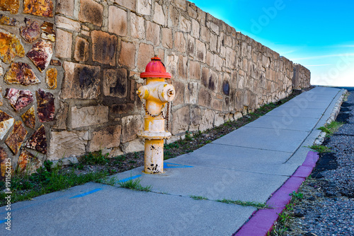 Colorful Fire Hydrant On Sidewalk Beside Rustic Stone Wall Under Clear Blue Sky