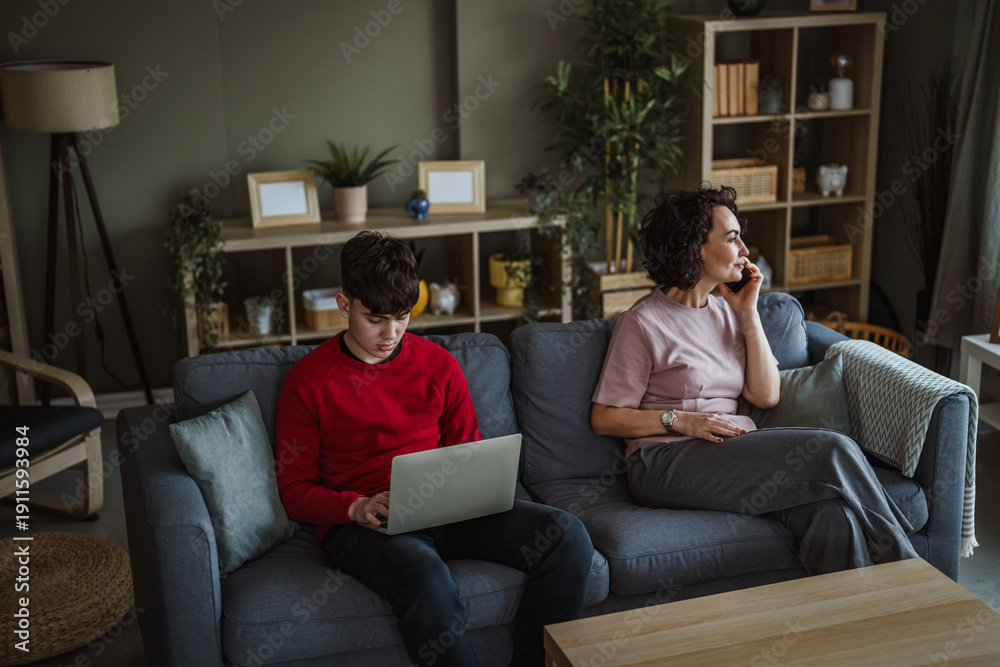 Obraz premium Mother and teenage son using devices on sofa