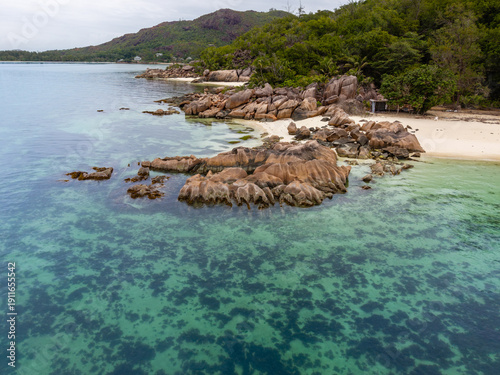 Aerial view of turquoise waters gently caress rugged rocks and pristine sands, a tranquil island paradise unfolds, Baie Ste Anne, Praslin, Seychelles.