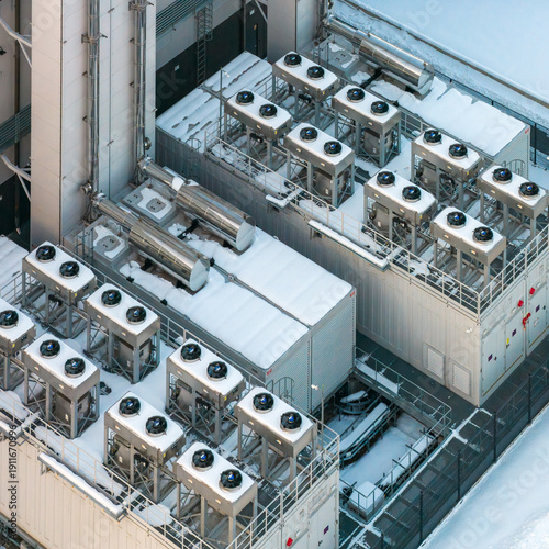 Aerial view of a snow dusted industrial rooftop bristling with ventilation units and complex ductwork, gleaming against the stark white backdrop, Duchnice, WojewÃ³dztwo mazowieckie, Poland.