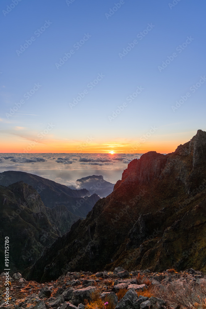 Fototapeta premium Sunrise above cloud sea and rugged peaks at Pico do Arieiro Madeira Portugal, warm light reveals volcanic ridges and deep valleys seen from mountain viewpoint at dawn