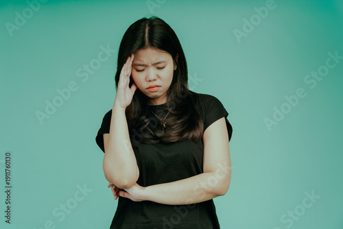 Asian woman suffering from headache desperate, stressed because pain and migraine. Female touching her temples feeling stress isolated on green background. Girl suffering from headache. Cold symptoms.