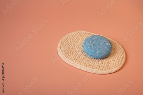Minimalist still life featuring natural soap and shampoo bars displayed with a loofah soap pad against a soft pastel background. The image highlights sustainable personal care 