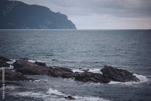 Foto Waves crash against dark, jagged rocks as a stormy sky looms overhead