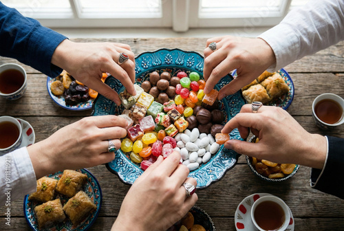 Top down view of family hands reaching for traditional sweets and Turkish delight from a blue bowl during eid mubarak celebration