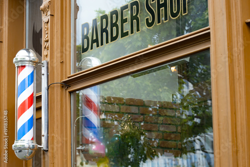 Vintage barber shop exterior featuring classic red and white striped pole, large window displaying the words 
