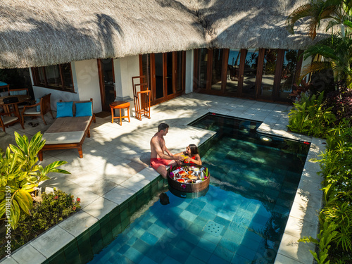 Aerial view of a couple in the pool with a floating tray of food surrounded by lush greenery near the building, Prince Maurice, Flacq District, Mauritius.