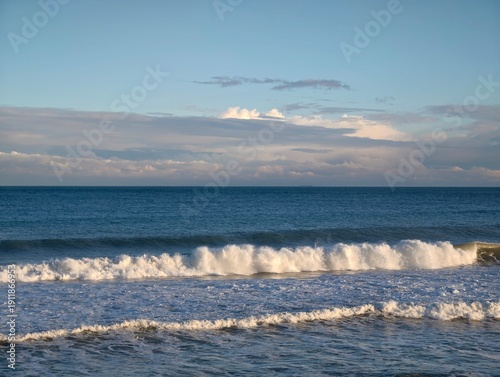 фотографія White crests roll over sandy beaches vibrantly, Dynamic ocean waves break with f