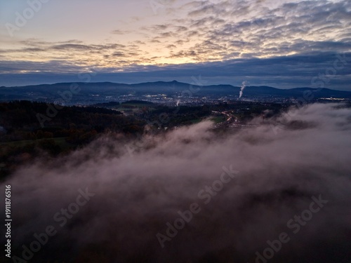 Fotografie aerial shot portraying sunrise through clouds over misty valley with glowing cit