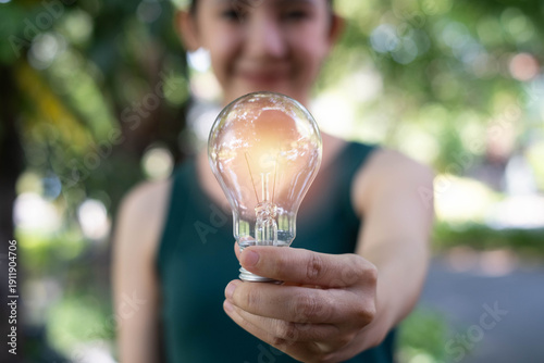 Εκτύπωση καμβά Smiling woman holding a glowing light bulb outdoors, symbolizing bright ideas, creativity, innovation, inspiration, energy efficiency, positive thinking, and future business or technology solution
