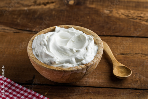 Plain greek yogurt in wooden bowl on wooden board