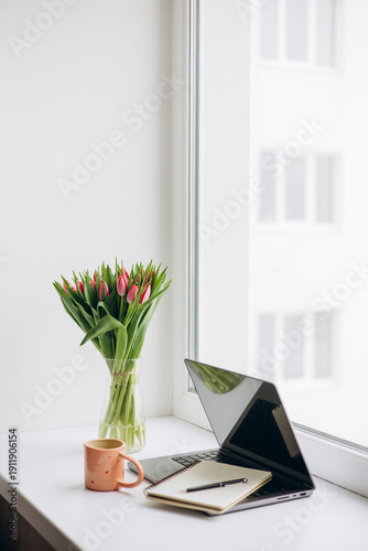 Remote work desk with laptop tulips and coffee by window, copy space.