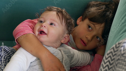 Canvastavla Older sibling cuddling baby on the couch, tender moment with the baby looking jo