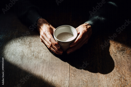 A minimalist photo showing only the hands of an elderly man holding a ceramic cup.