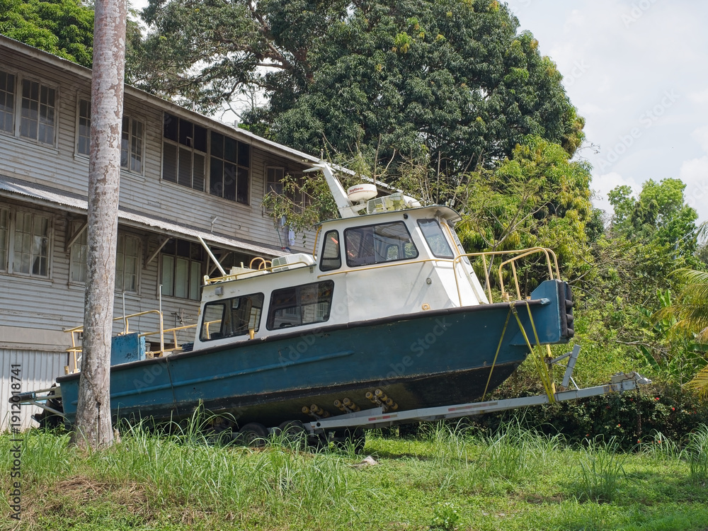 Obraz premium Green and white tourist boat on trailer beside wooden tropical pier building with palm trees