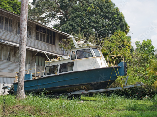 Green and white tourist boat on trailer beside wooden tropical pier building with palm trees