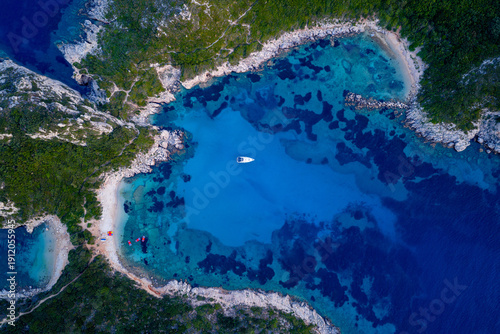 Tableau sur toile Zenith aerial view of a solitary white yacht moored in the transparent, turquoise waters of a secluded bay at Porto Timoni, Corfu, surrounded by a dramatic, rocky shoreline