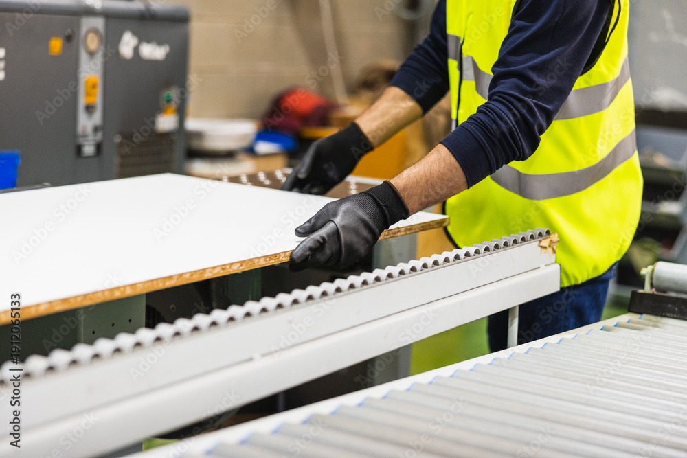 Fototapeta premium Worker handling wood panel on rollers in factory