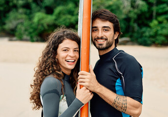 Portrait of a young couple surfing at the beach, holding surfboards, having fun together ocean waves, healthy life holidays adventure concept