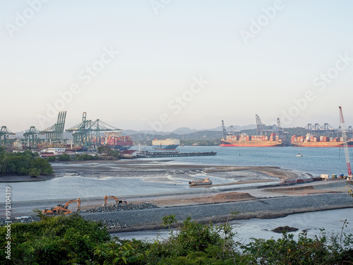 Tropical port landscape with gantry cranes, container ships, and waterfront construction at golden hour (wide view)