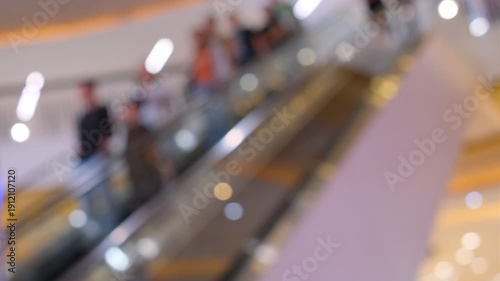 A blurry image of a crowded mall with people walking on escalators. Scene is busy and bustling, with people moving quickly and the escalators providing a sense of movement and energy