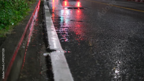 A street with a white line and a car driving by. The street is wet and the car is black