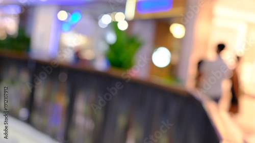 A blurry image of a mall with people walking around and a few potted plants
