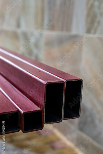 Red painted steel square tubes stacked outdoors, symbolizing construction materials, metal industry, structural engineering and building framework concept