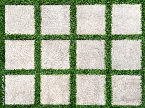 Cuadro en lienzo Close up of white paving stone tiles in square grid pattern with green grass growing separating the square paving stone