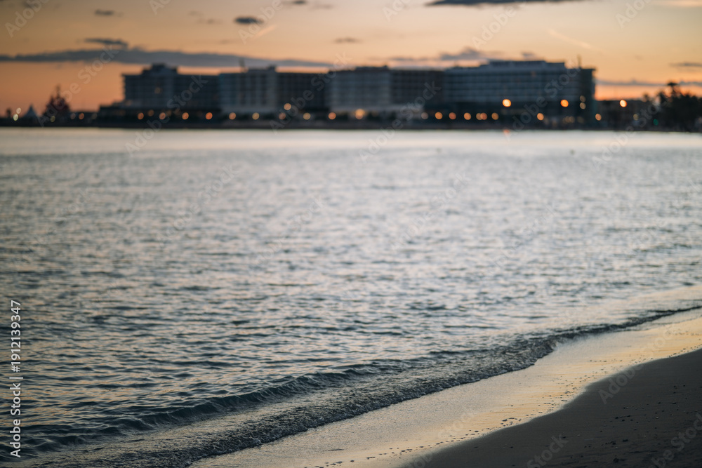 Fototapeta premium Beach coastline at dusk with distant city buildings