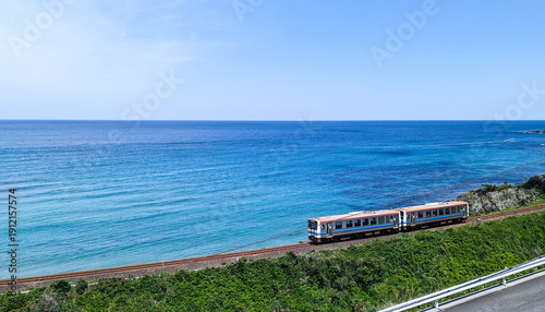 Φωτογραφία 夏の青空の下、美しい海岸線沿いを走行する2両編成の汽車（右側配置）