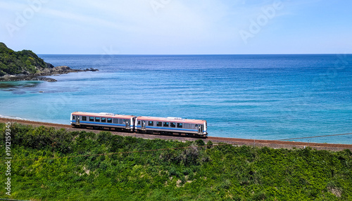 エメラルドグリーンの海を背に走るローカル列車（中央配置・日本の夏）