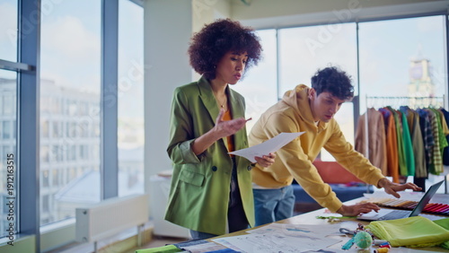 Fashion studio executive talking to designer explaining design task in workshop.