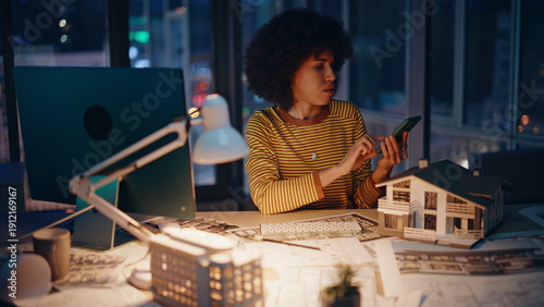 Night manager working construction project overtime checking time on cellphone.