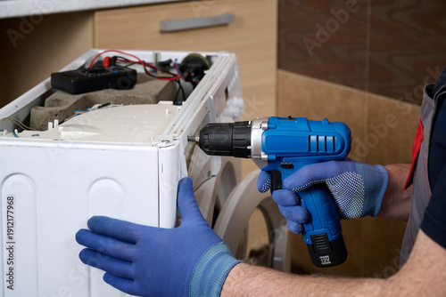Bild auf Leinwand Close-up of a home appliance repair technician disassembling a washing machine with a power screwdriver