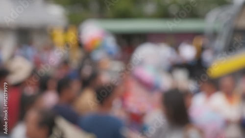 A blurry image of a crowd of people with some holding balloons. Scene is lively and festive