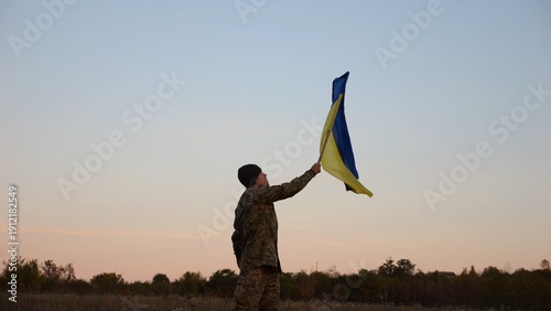 фотографія Male military waving blue-yellow banner on liberated territory occupied by russia