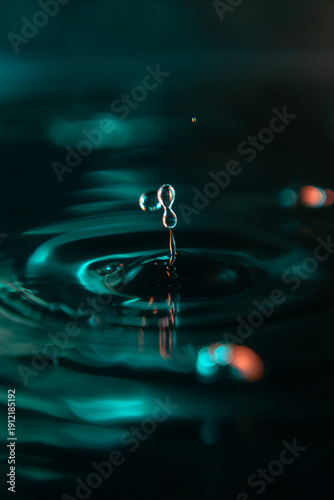 A stunning macro shot of a water drop falling into a liquid surface, creating elegant ripples. High contrast teal and orange colors on a black background. Ideal for creative design and wallpapers.