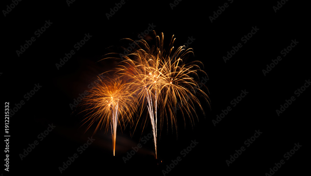 Fototapeta premium Vibrant fireworks exploding in the night sky with bright orange sparks and streaks of light against a dark background